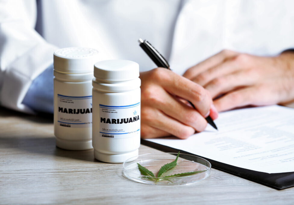 Doctor writing on prescription blank and bottle with medical cannabis on table close up